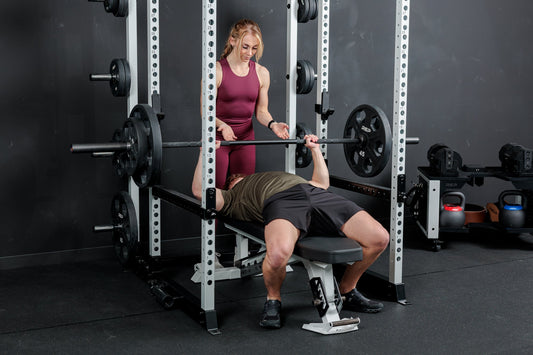 An athlete does bench press in the Altitude™ rack with a spotter behind.