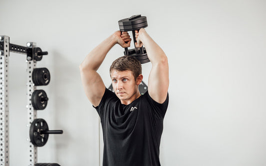 A man does a tricep over-head extension with an adjustable dumbbell.