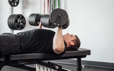 Athlete does chest press on a bench with adjustable dumbbells.