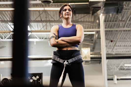 An athlete stands with her arms crossed and a belt squat belt around her hips.