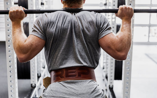 An athlete prepares to squat with a REP leather lifting belt around his waist.