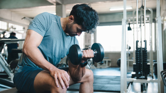 A trainee seated on a bench performing a concentration curl with a dumbbell.