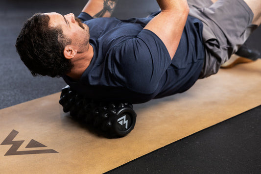 A man uses a foam roller to roll out his upper back.