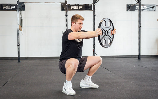Athlete squats with a weight plate.
