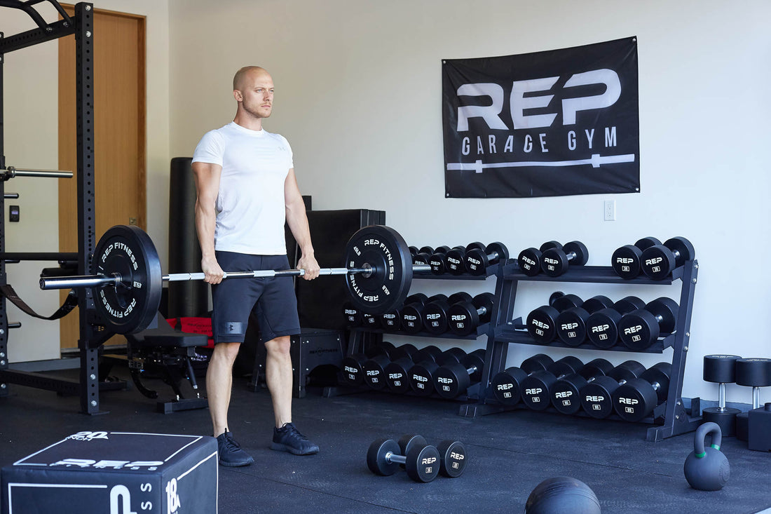 A man lifts a barbell in a home gym stocked with dumbbells and other gym equipment.