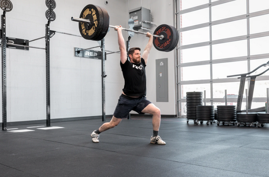 A man performs a clean and jerk using a barbell in a gym.