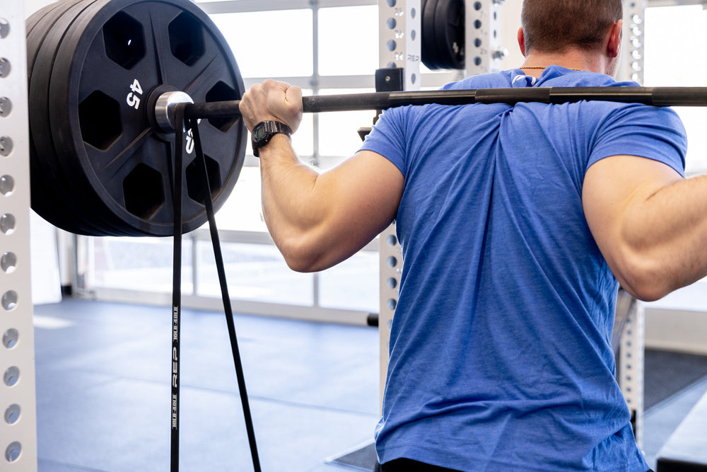 Athlete using a pair of black Latex-Free Pull-Up Bands for added resistance while barbell back squatting.