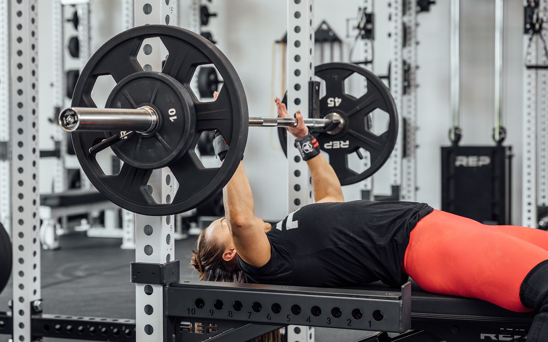 Female lifter preparing to perform a bench press with a loaded REP Double Black Diamond Power Bar.