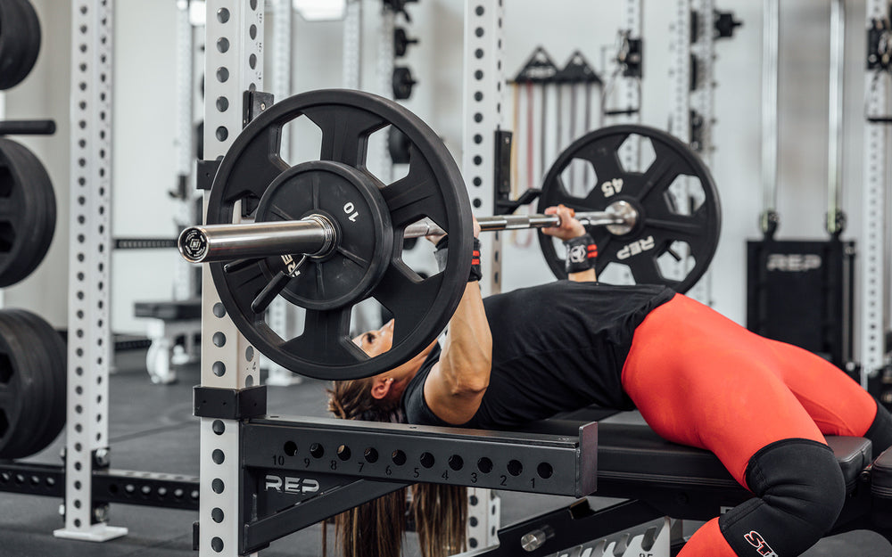 Female lifter performing a bench press with a loaded REP Double Black Diamond Power Bar.