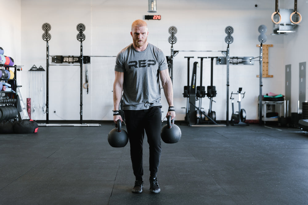 Lifter deadlifting a pair of kettlebells while wearing REP Lifting Straps.