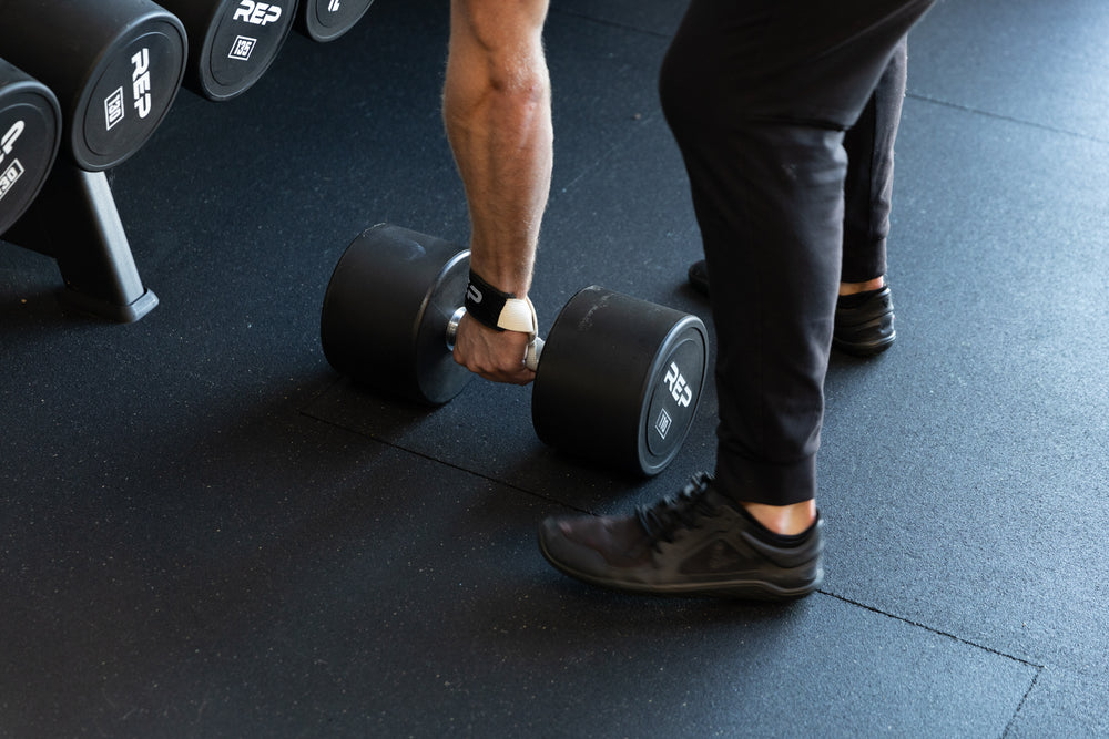 Lifter securing his REP Lifting Strap to the handle of a heavy dumbbell.