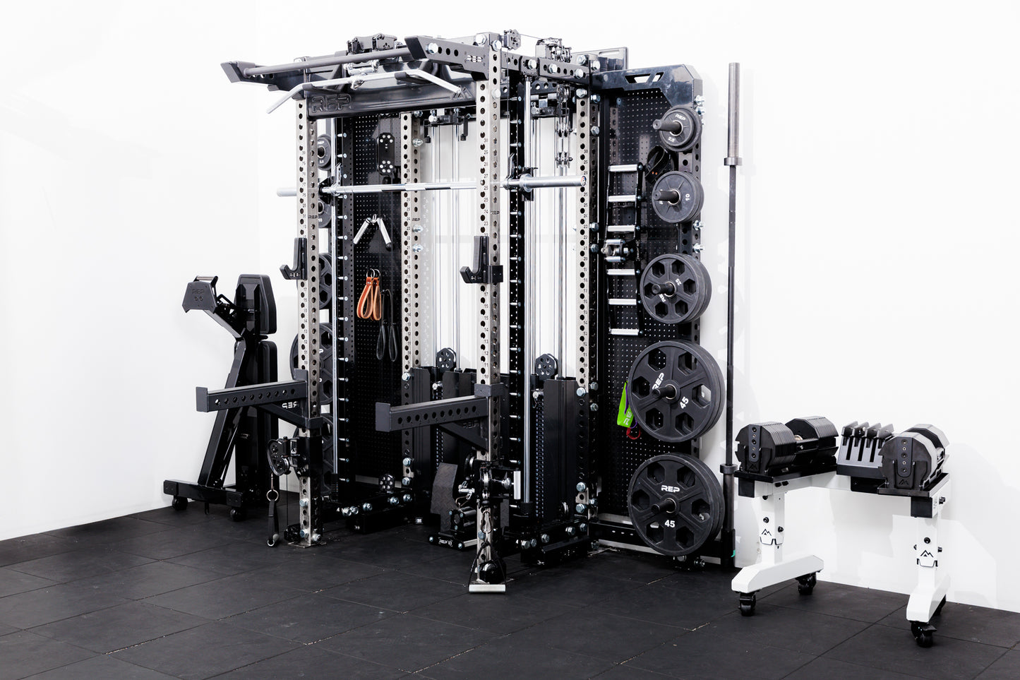 Gym equipment including a Smith machine rack attachment  on a Summit™ All-In-One Ares™ 2.0 Wall-Mounted and weight rack on a black floor with white walls.
