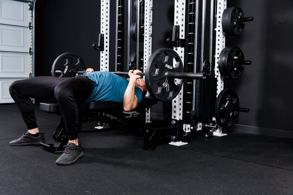 Person performing bench press with a barbell and weights on the Summit™ All-In-One Athena™ .