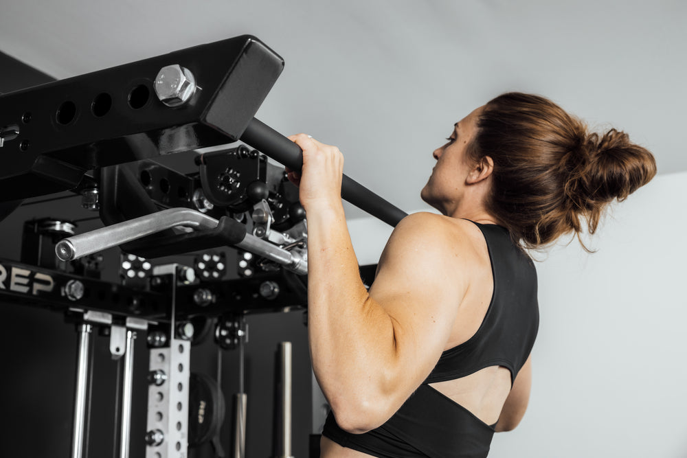 Person performing pull-ups on a pull-up bar (Ares 2.0 4-Post Pull-Up Bar + Pull-Up Bar Extension Brackets) against a plain background.