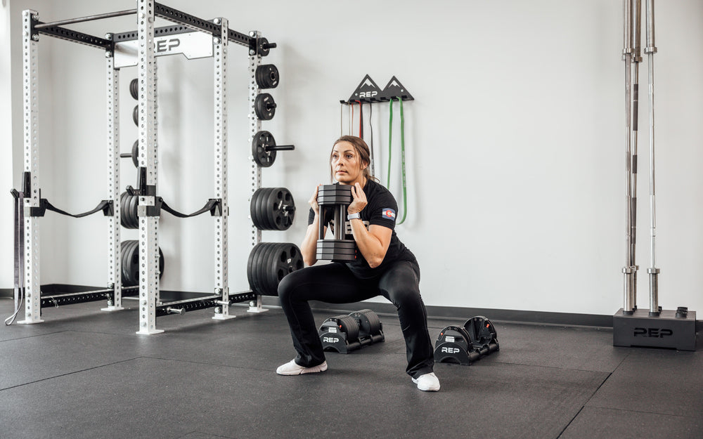 Female lifter performing a goblet squat with a single REP Fitness QuickDraw Adjustable Dumbbell.