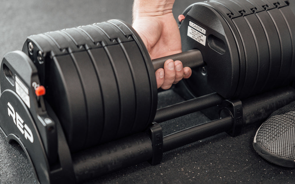 Lifter gripping the fully knurled handle and preparing to lift the REP Fitness QuickDraw Adjustable Dumbbell out of it's cradle.