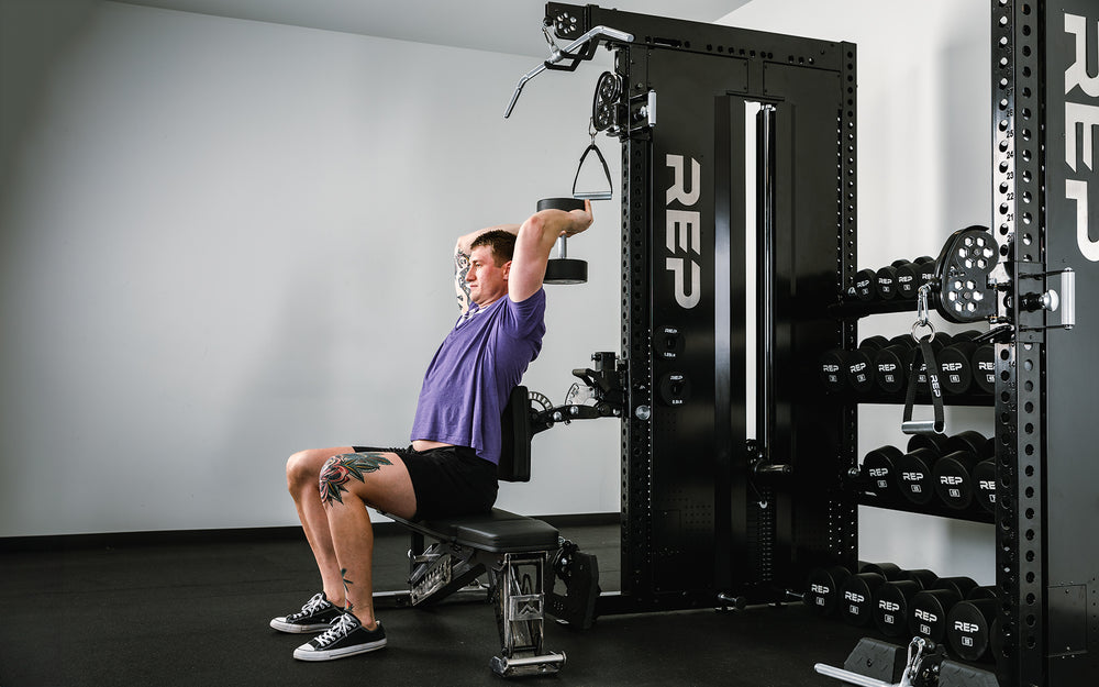 Man sitting on a bench using the Pegasus™ Attachment connected to the Adonis™ doing tricep exercises.