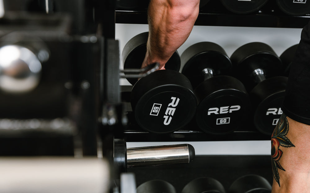 Someone picking up dumbbells stored on the storage shelves of the Dual Adonis™ with Storage setup.