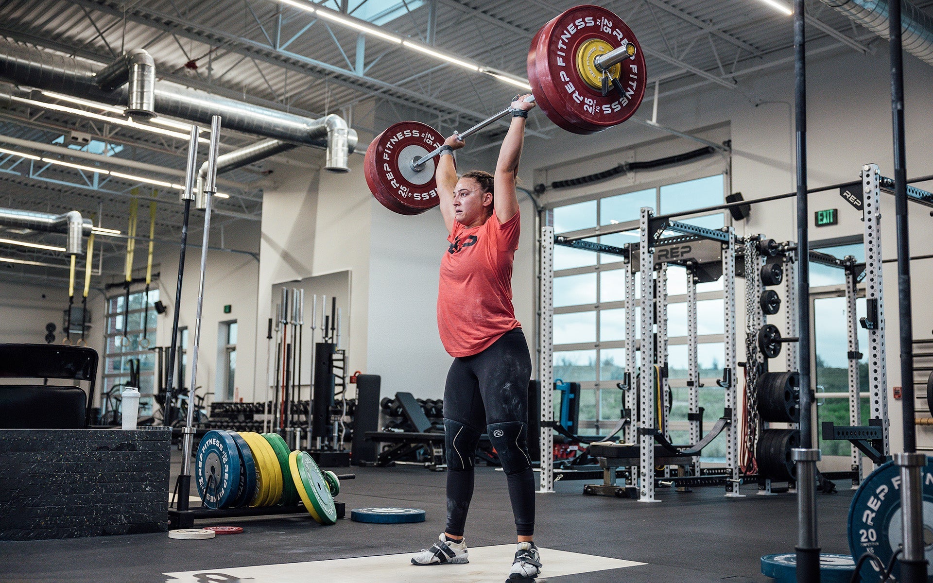 Female lifter performing a clean and jerk on an Olympic lifting platform using REP's 15kg Alpine Weightlifting Bar.