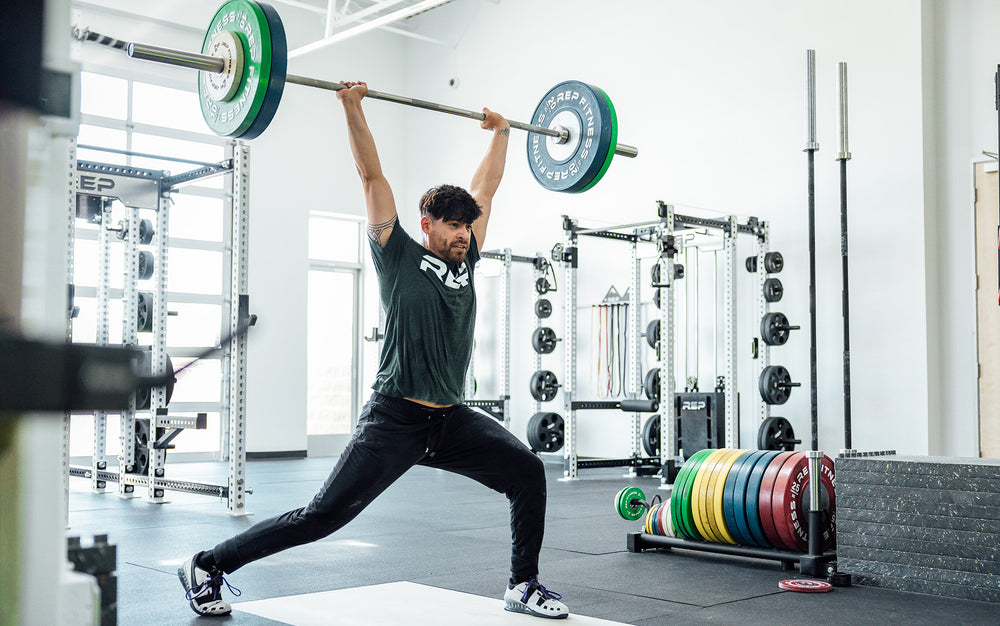 Male lifter performing a split jerk on an Olympic lifting platform using a REP 20kg Alpine Weightlifting Bar.