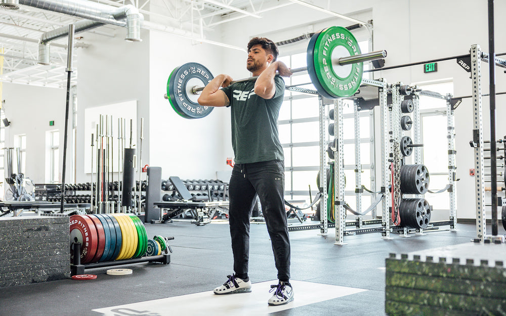 Male lifter at the top of a clean and jerk on an Olympic lifting platform using a REP 20kg Alpine Weightlifting Bar.