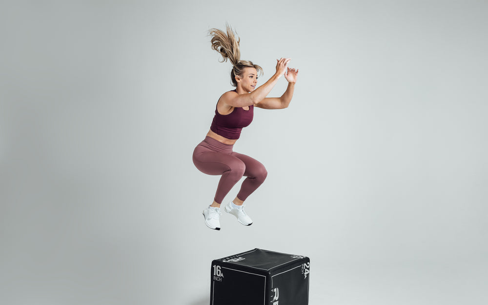 Side shot of an athlete mid-movement performing a box jump while wearing the REP Rhea Tank in Wine.
