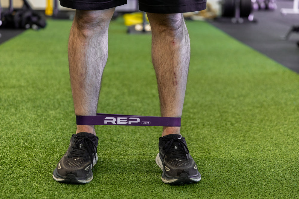 Athlete using a purple short resistance band around his lower leg for agility exercises.