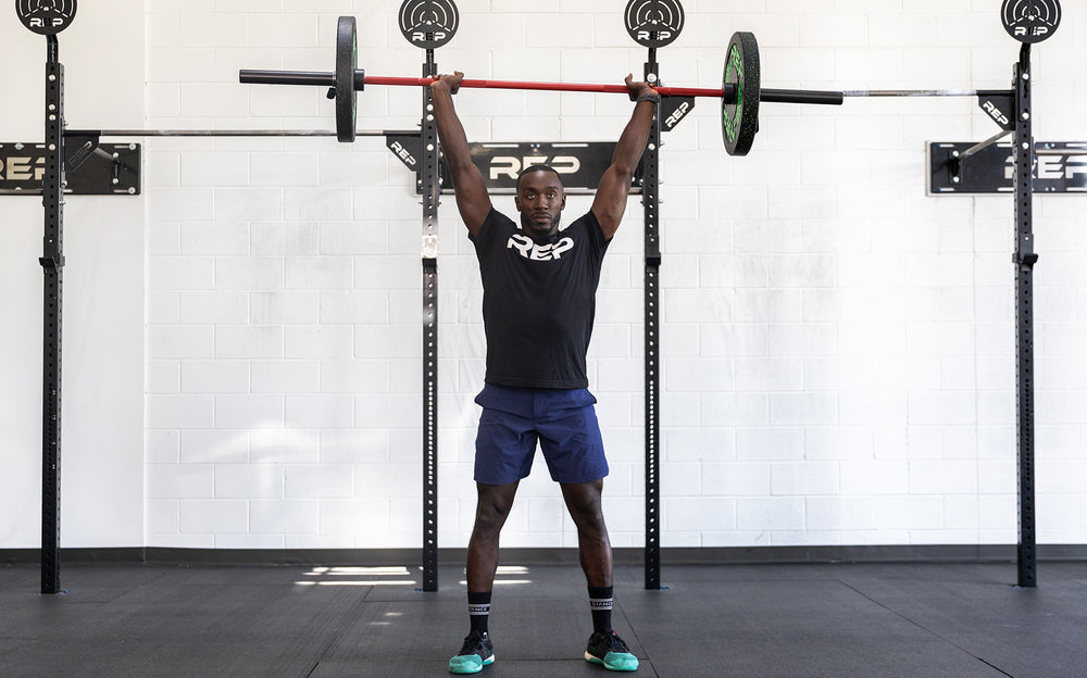 Male lifter holding a loaded REP 20kg Colorado Bar in the overhead position.