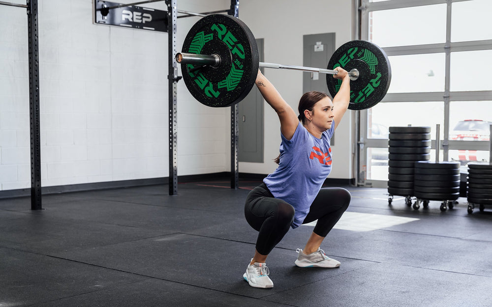 Female lifter in the bottom receiving position of a snatch using a loaded REP 15kg Black Canyon Bar.