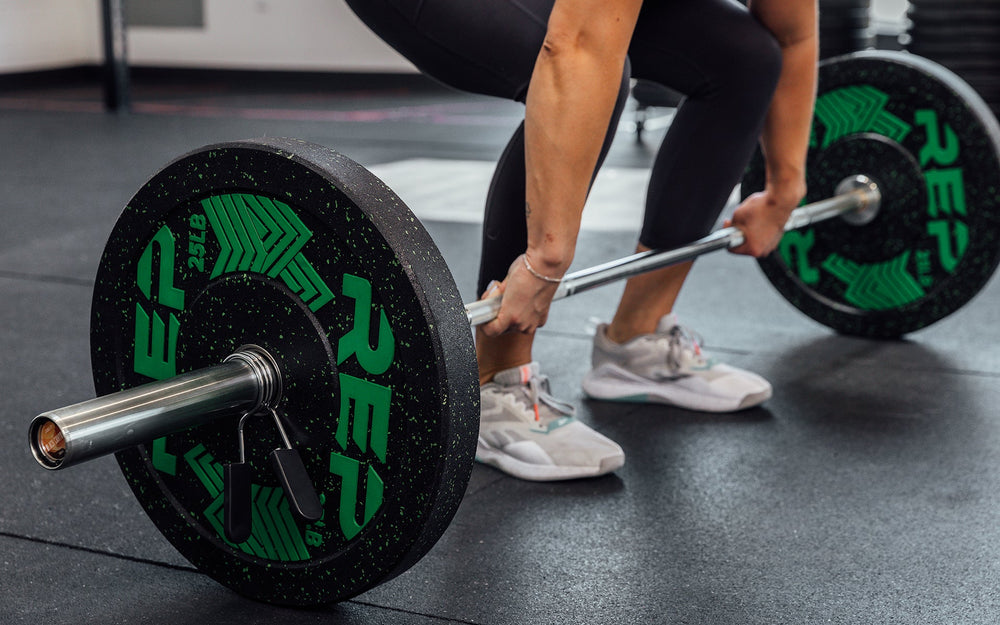 Female lifter preparing to perform a power clean with a loaded REP 15kg Black Canyon Bar.