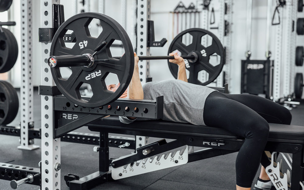 Female lifter performing a bench press with a loaded REP 15kg Colorado Bar.