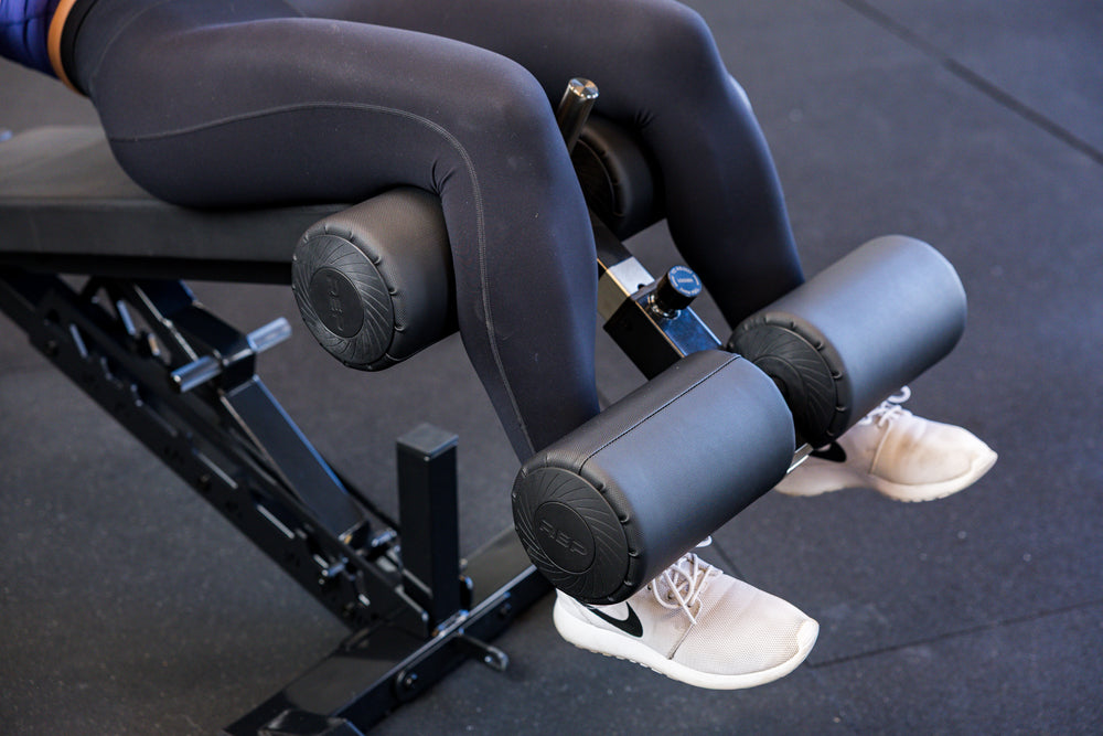 Close-up of an athlete's legs secured in the Adjustable Bench Leg Roller Attachment 2.0