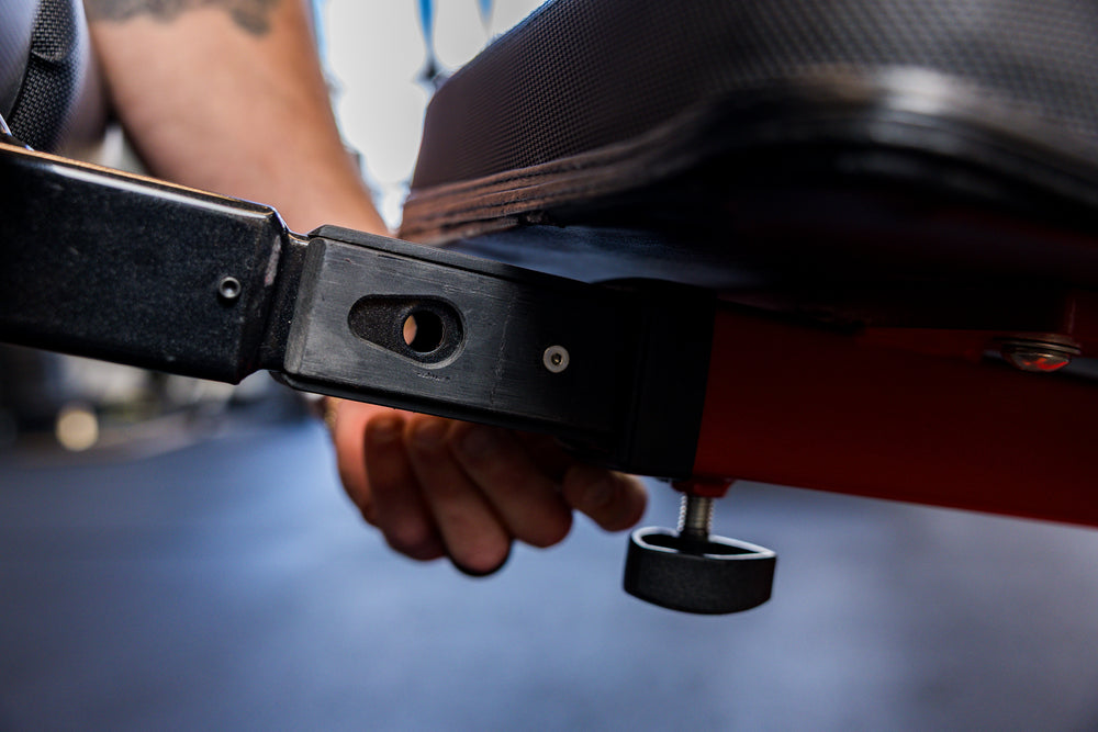 Close-up of an athlete installing the Adjustable Bench Leg Roller Attachment 2.0 into the bench's receiver