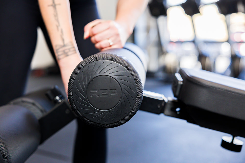 Close-up of an athlete installing the Adjustable Bench Leg Roller Attachment 2.0
