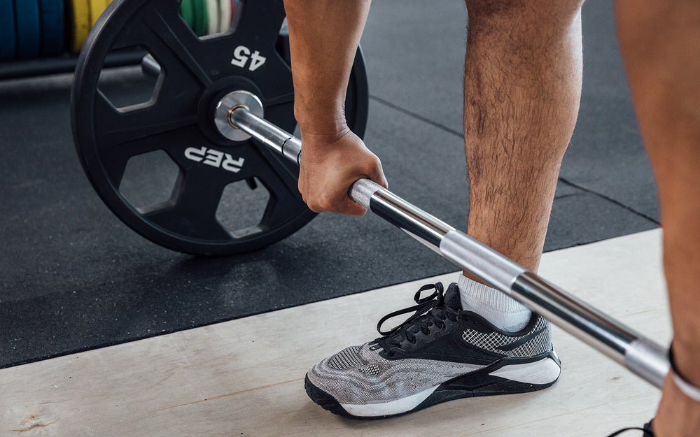 Close-up view of a male lifter getting a grip on a loaded REP Delta Basic Bar on an Olympic lifting platform.