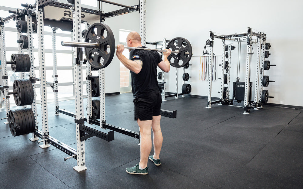 Male lifter with a loaded REP Double Black Diamond Power Bar in the back rack position.