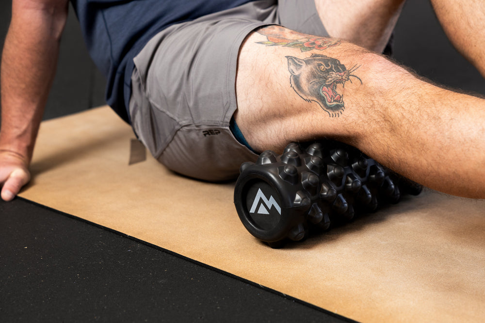 Person using High Density Foam Roller to roll out hamstring on a cork yoga mat.