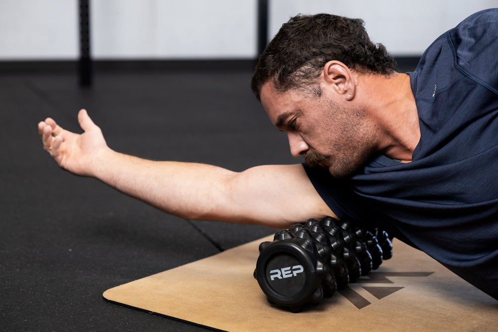 Person using High Density Foam Roller to roll out tricep on a cork yoga mat in gym setting