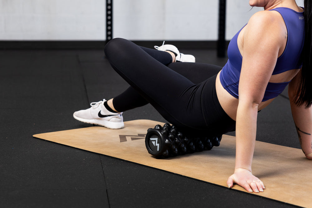 Person using a foam roller  for glutes on a mat in a gym setting