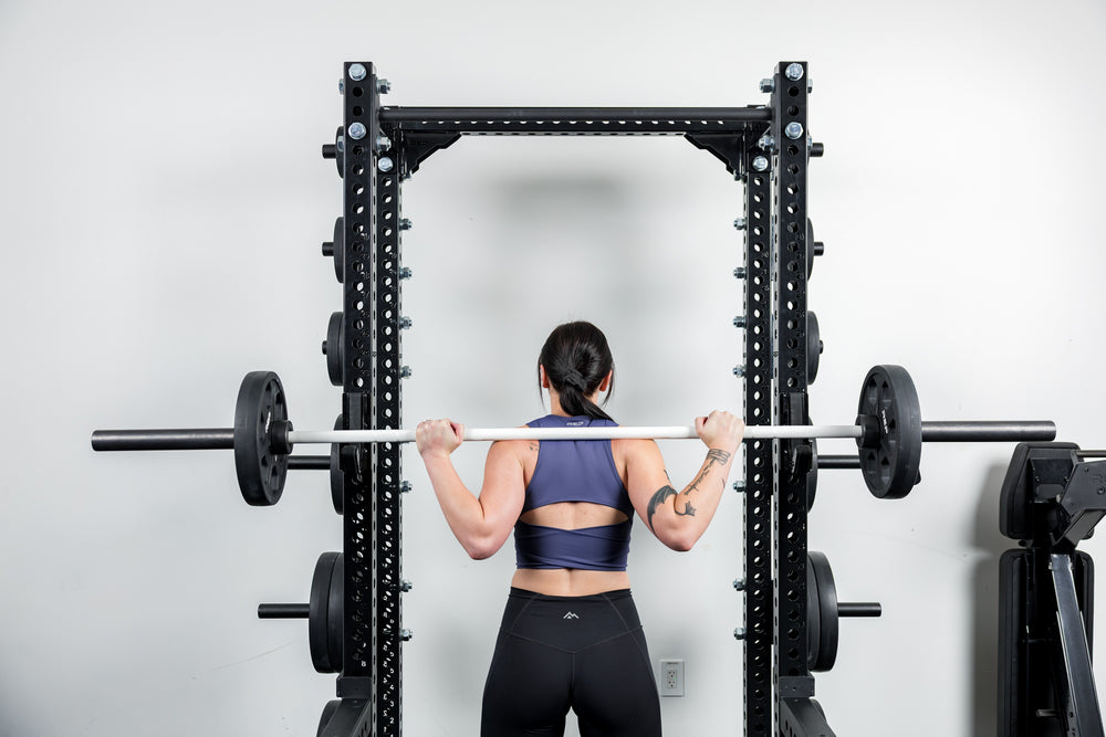 Person lifting a barbell in a gym setting featuring a REP power rack with the compact Logo Plate Crossmember 2.0