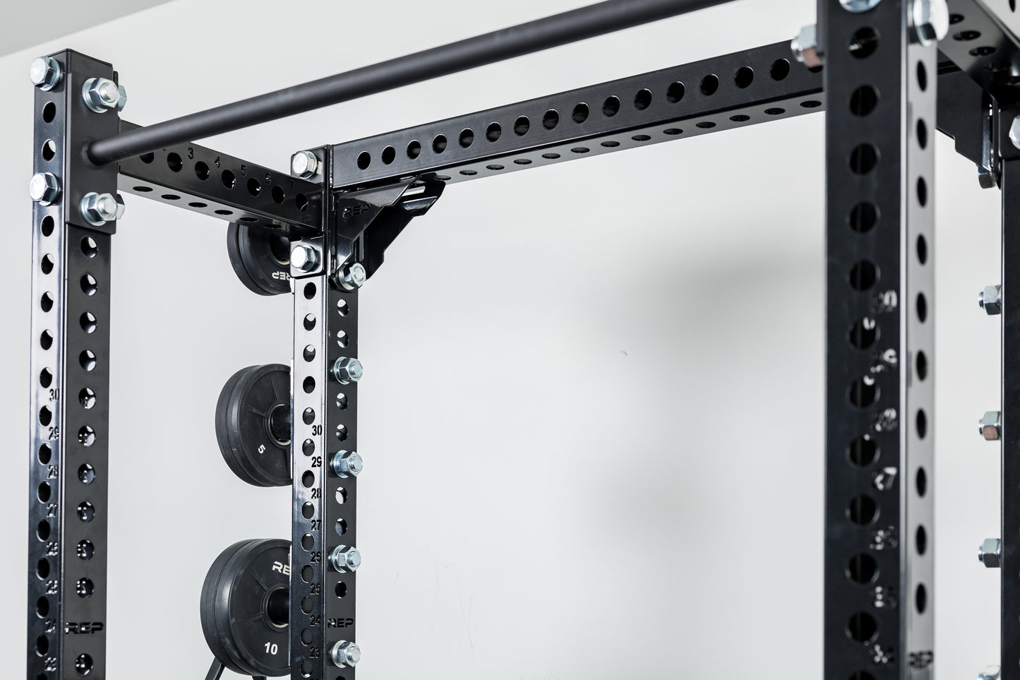 Close-Up of Compact Logo Plate Crossmember 2.0 on a REP power rack with weights on a white background.