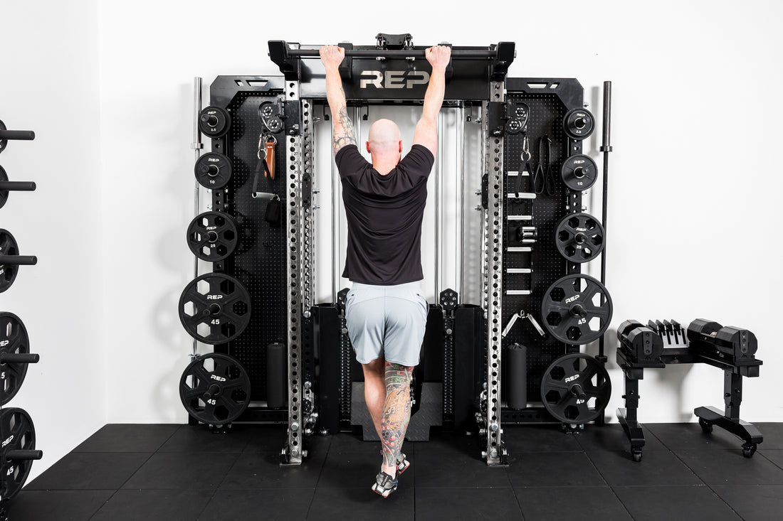 Person using a Rep Fitness power rack in a gym setting with the standard Logo Plate Crossmember 2.0 shown - black with laser-cut "REP".