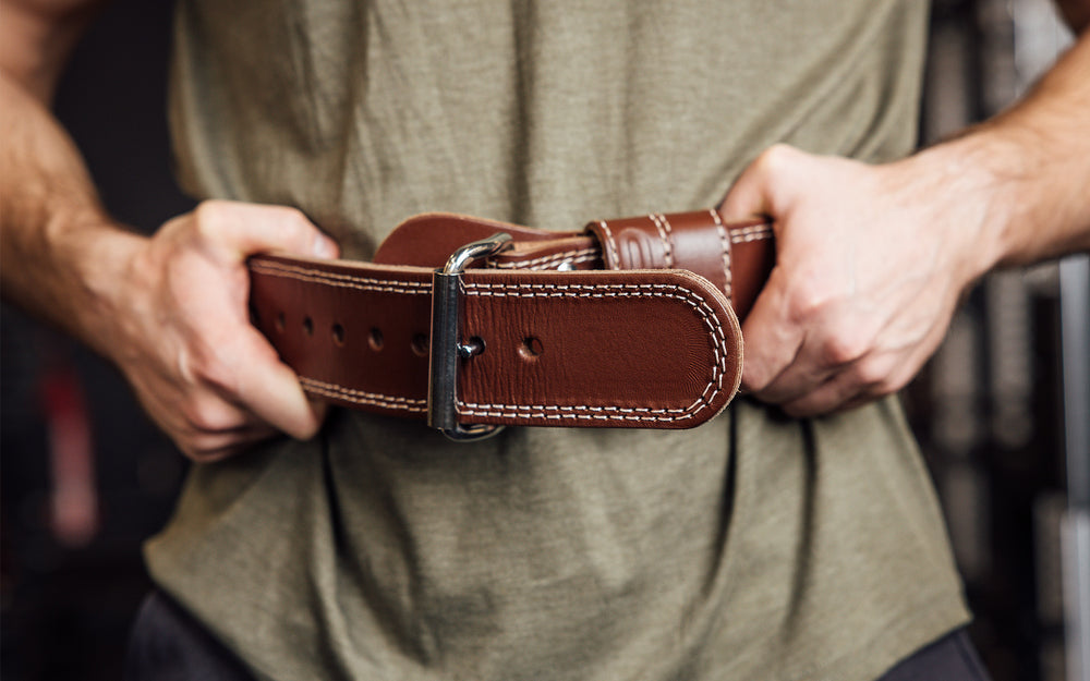 Close-up front view of athlete putting on the brown REP Leather Olympic Lifting Belt.