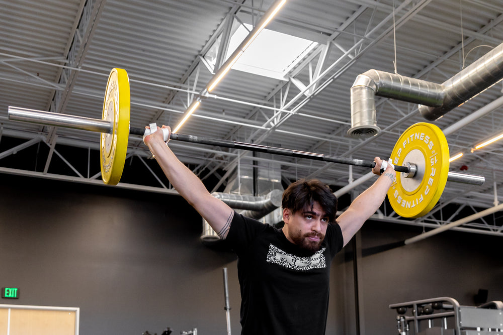 Front view of an athlete at the finish position of a snatch while wearing a pair of white REP Olympic Lifting Straps.