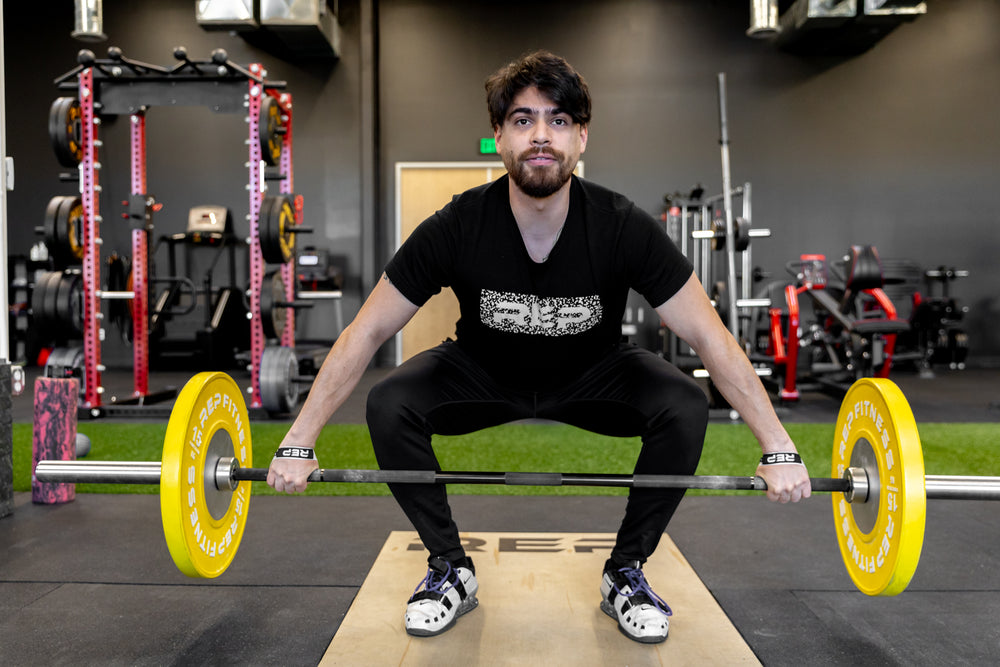 Front view of an athlete at mid-shin level of a snatch while wearing a pair of white REP Olympic Lifting Straps.