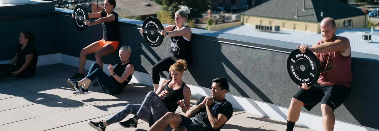 Group fitness class working out on a rooftop performing sit-ups and wall sits.
