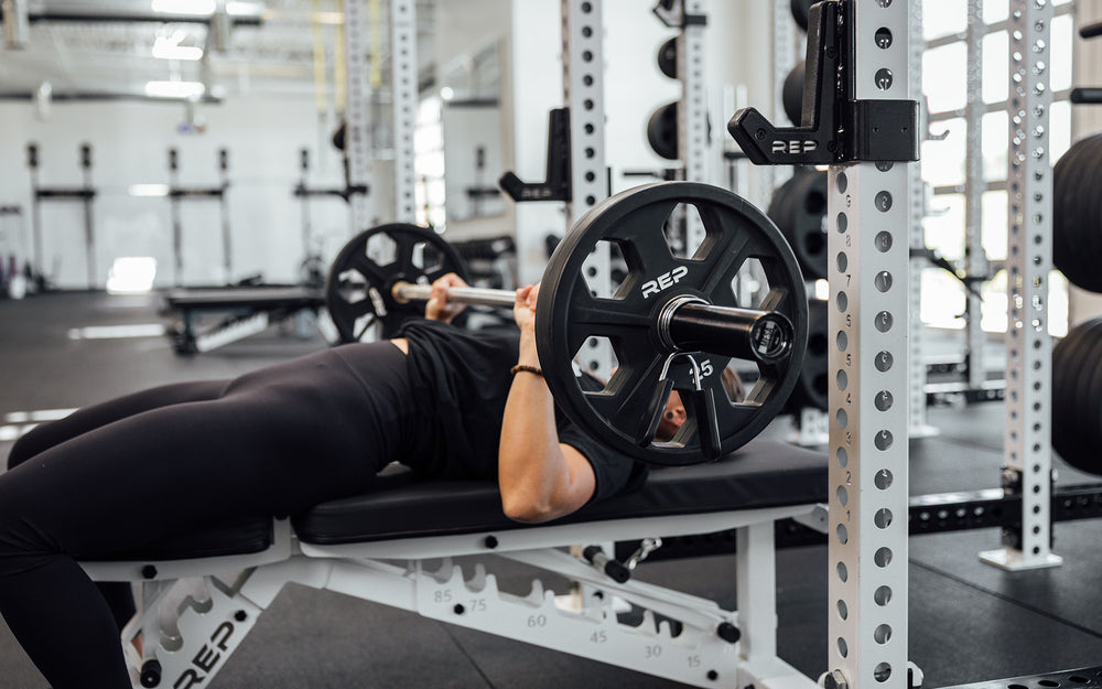 Female lifter performing a bench press with a loaded REP Mesa Technique Bar.