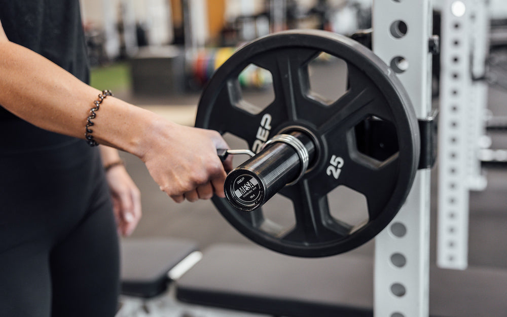 Female lifter putting a spring clip on a racked REP Mesa Technique Bar.