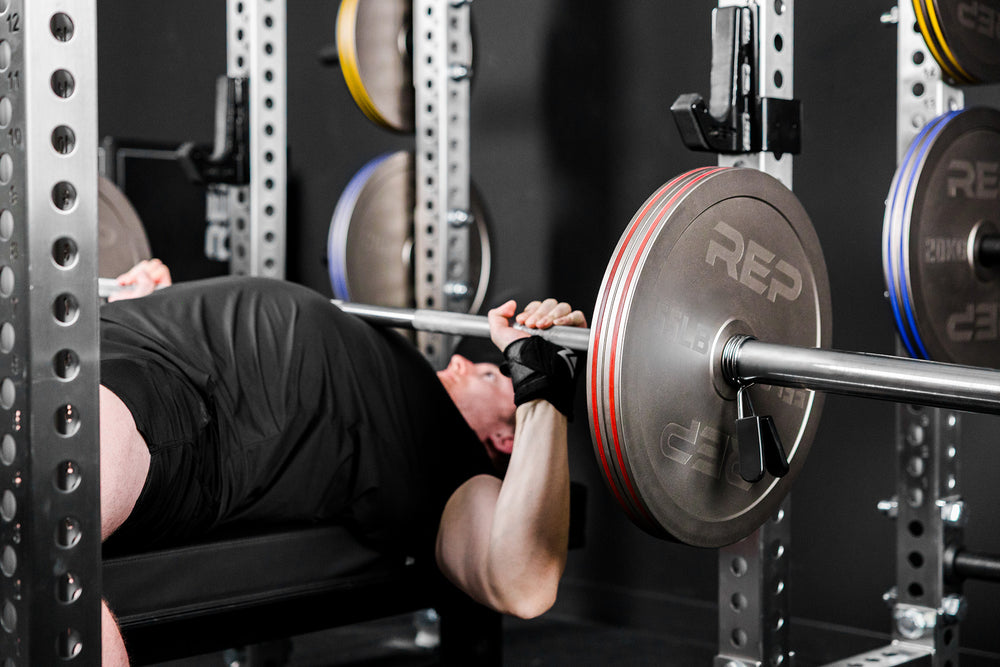 An athlete bench pressing in a PR-5000 rack with Rep Fitness Calibrated Steel Plates (LB) loaded on the barbell