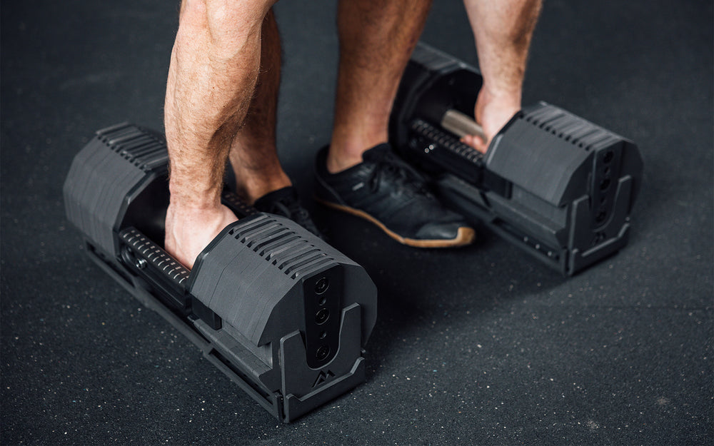 Close-up view of an athlete gripping the handles and preparing to lift a pair of REP x PÉPIN  FAST Series Adjustable Dumbbells out of their cradles.